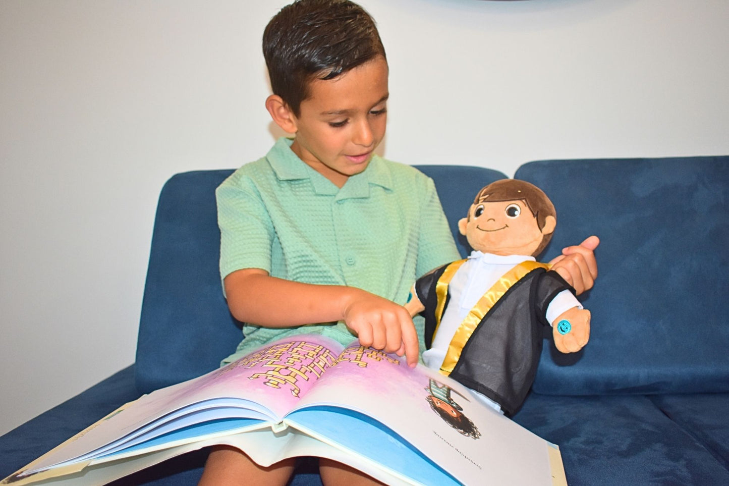 Child reading a book with a muslim doll on a blue couch. Close-up of Khaled doll’s smiling face. Muslim plush toy for toddlers.