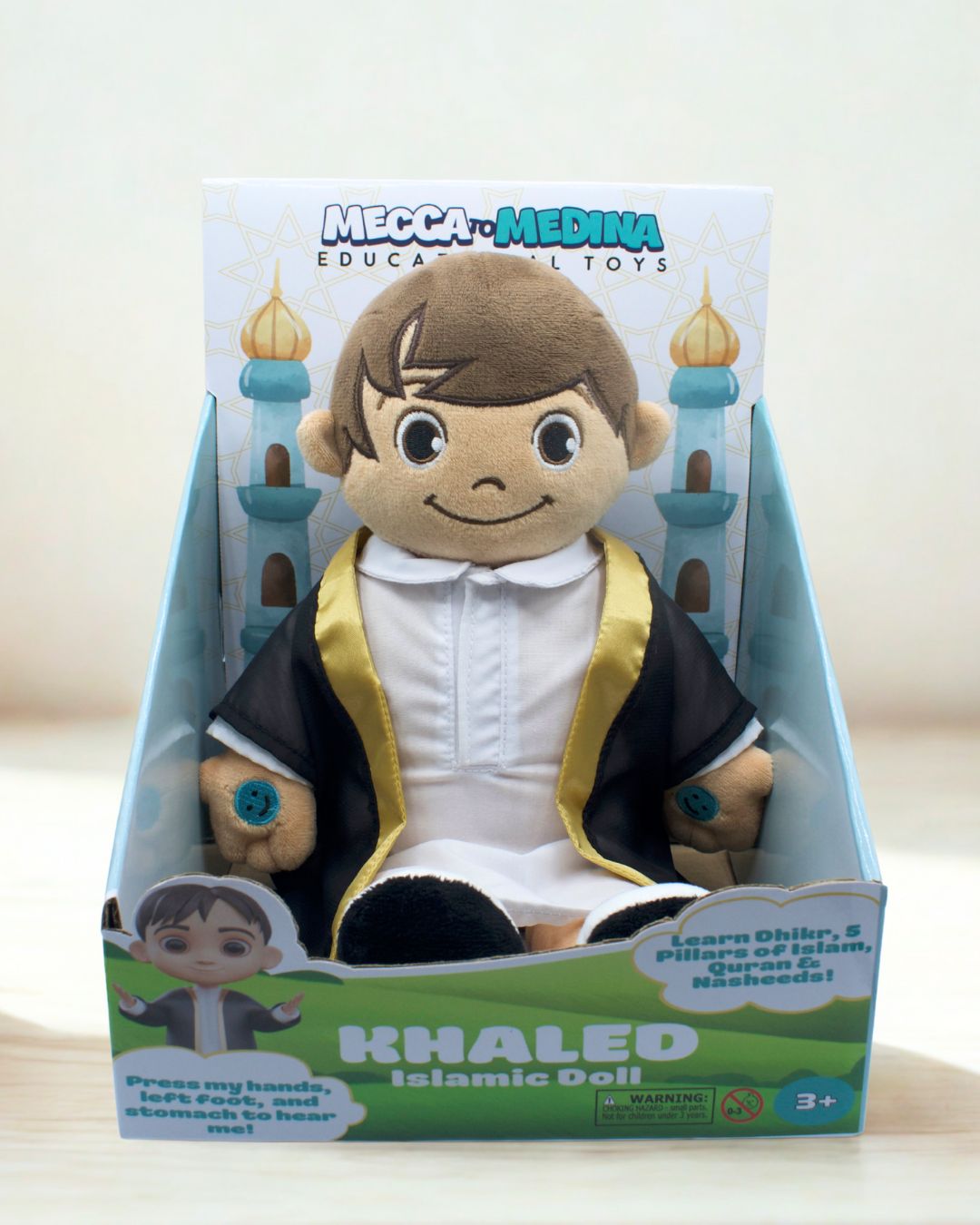 Plush toy in packaging with 'Mecca to Medina' branding on a light background. Khaled plush toy sitting upright. Educational Islamic doll for kids learning Islam.