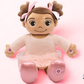 Madina Islamic Teaching Plush toy resembling a baby with brown hair and pink bows on a pink background. Muslim doll with hijab Madina reciting Surah Al-Fatiha