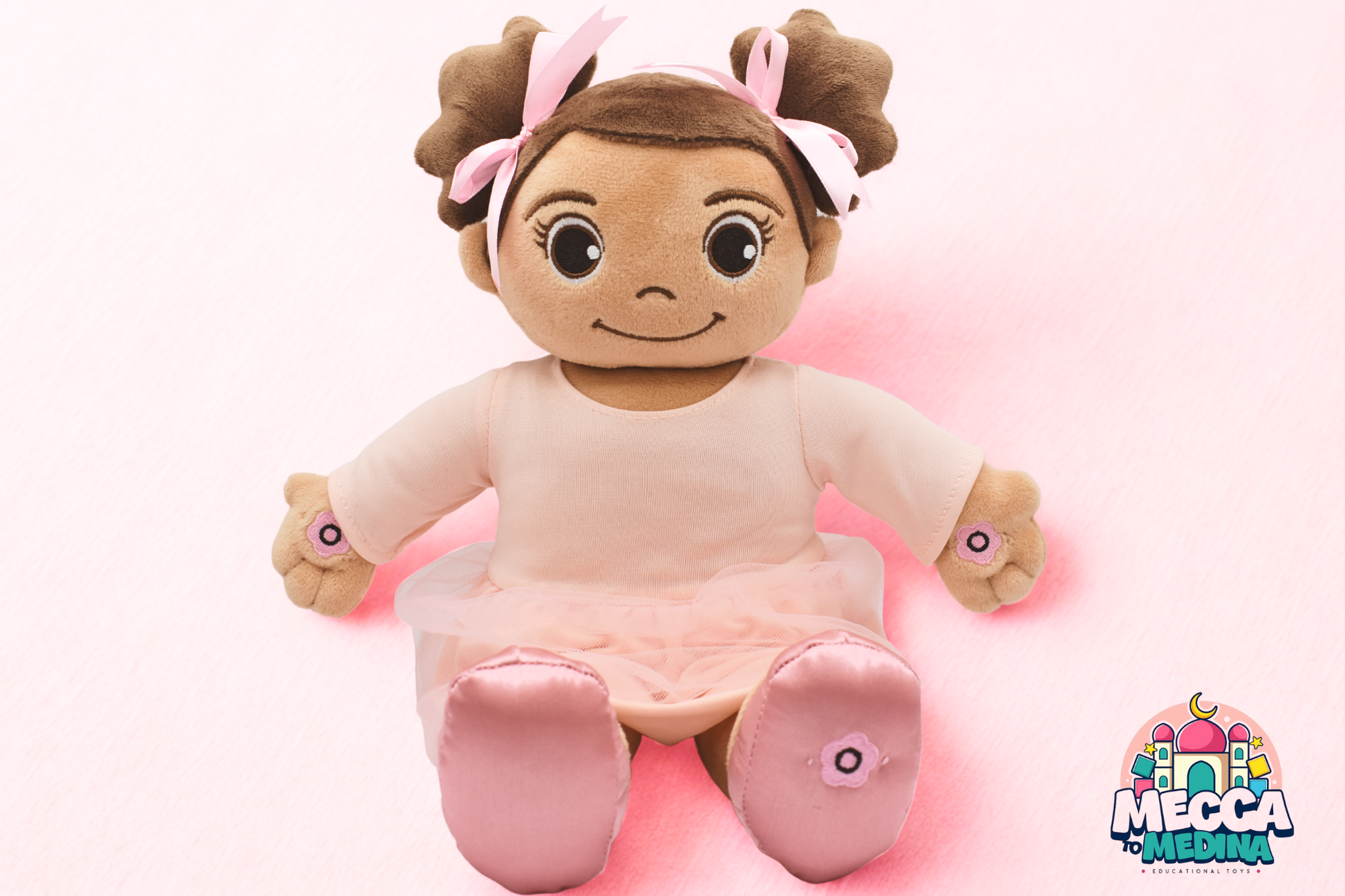 Madina Islamic Teaching Plush toy resembling a baby with brown hair and pink bows on a pink background. Muslim doll Madina reciting Surah Al-Fatiha